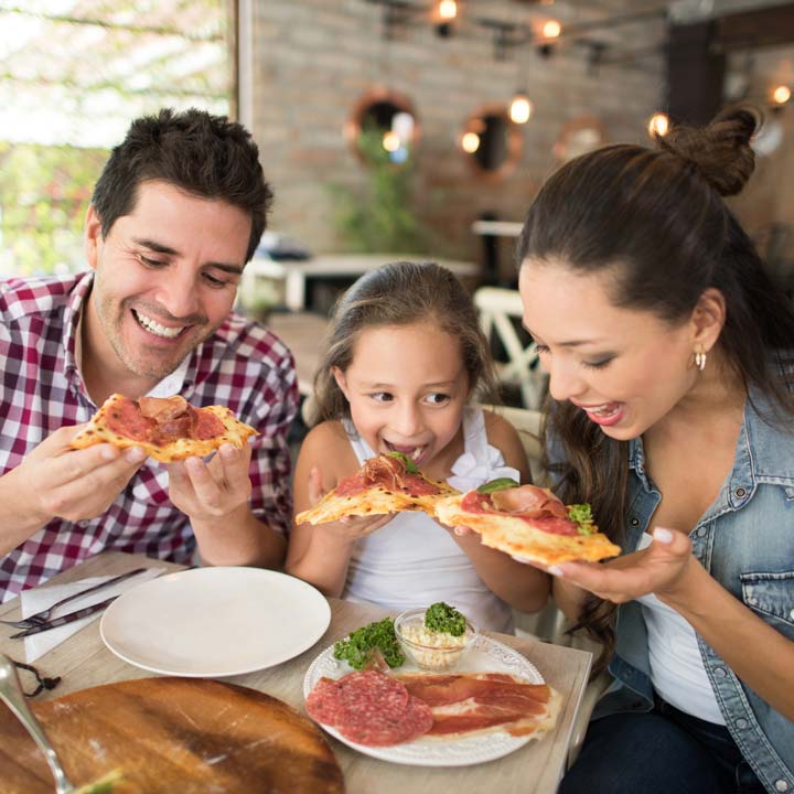 Happy Latin American family eating pizza at an Italian restaurant