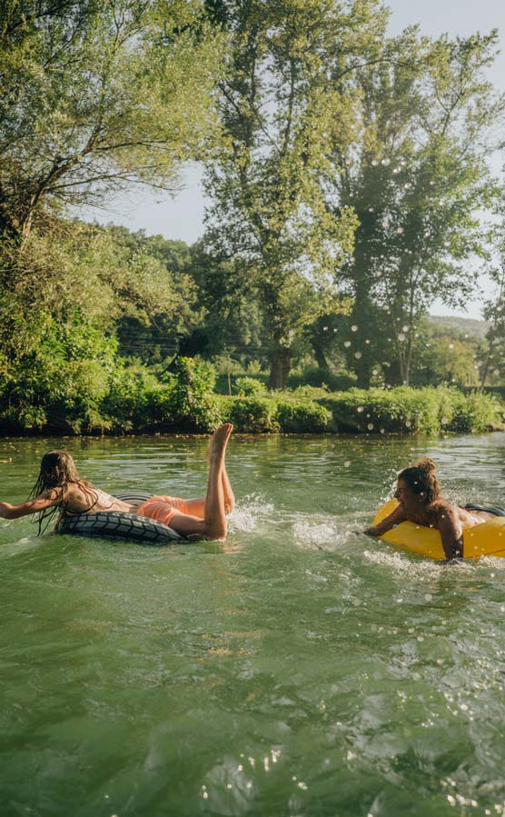 Photo of teenage girls swimming in the river while hanging out in nature; enjoying their youth and friendship and spending a hot summer day outdoors.